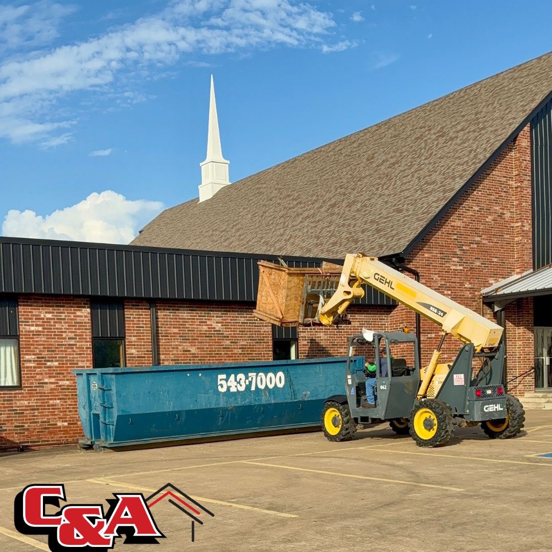 Commercial roofing tear-off with telehandler loading dumpster at church in Oklahoma